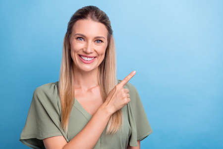 Photo of funny sweet young lady wear green outfit smiling pointing finger empty space isolated blue color backgroundの写真素材