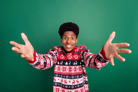 Photo of funny funky guy raise hands invite embrace wear print sweater isolated green color backgroundの写真素材