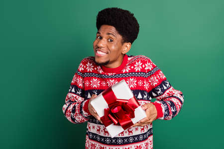 Photo of pretty funky guy dressed print pullover smiling holding gift box isolated green color backgroundの写真素材