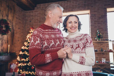 Photo portrait senior couple holding hands wearing red festive sweaters celebrating christmasの写真素材
