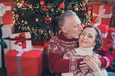 Photo portrait elder couple celebrating new year sitting near gift pile husband kissing wifeの写真素材
