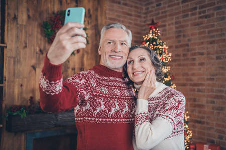 Photo portrait elder couple taking selfie together with new year presents in festive decorated apartmentsの写真素材