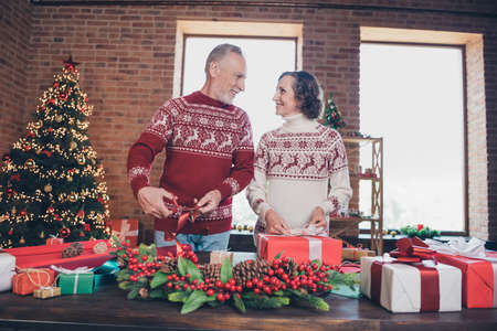 Photo of positive married couple wrapping x-mas presents man hold scissors wear ornament pullover home indoorsの写真素材