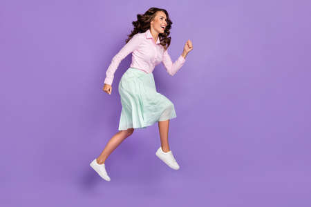 Full length profile photo of sweet young brunette lady run wear shirt skirt sneakers isolated on violet backgroundの写真素材