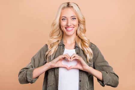 Photo of young girl happy positive smile show finger heart symbol love feelings isolated over beige color backgroundの写真素材