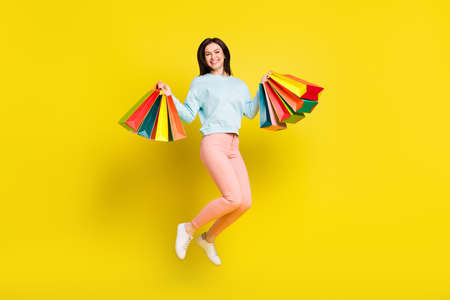 Profile full size photo of cool brown hairdo young lady jump with bags wear hoodie trousers isolated on yellow backgroundの写真素材