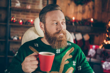 Photo of young dreamy attractive positive man hold hands cup coffee christmas eve indoors inside house homeの写真素材