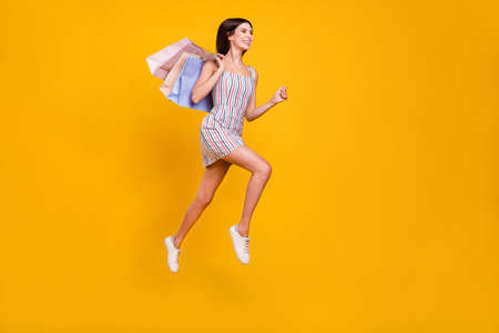 Full length body size woman smiling jumping running on sale with bags isolated vivid yellow color backgroundの写真素材