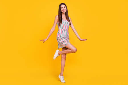 Full length body size woman smiling careless happy in striped dress isolated vivid yellow color backgroundの写真素材