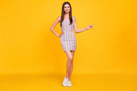 Full length body size pretty confident girl in dress smiling showing copyspace isolated vivid yellow color backgroundの写真素材
