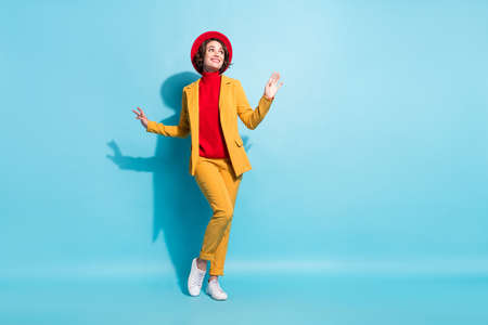 Photo of sweet charming young lady wear yellow blazer red cap smiling dancing looking empty space isolated blue color backgroundの写真素材