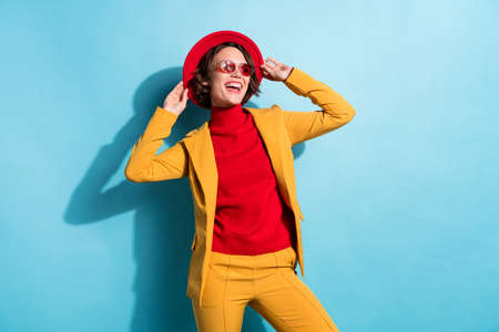 Photo of pretty charming young woman dressed red headwear glasses looking empty space smiling isolated blue color backgroundの写真素材