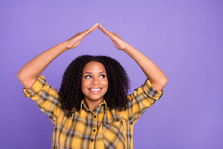 Photo of dreamy happy afro american woman look empty space hands roof above head isolated on purple color backgroundの写真素材
