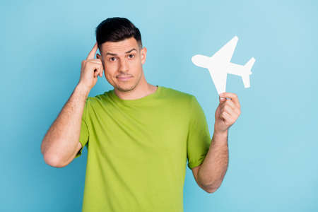 Photo portrait man in green t-shirt keeping paper plane thoughtful doubt isolated pastel blue color...