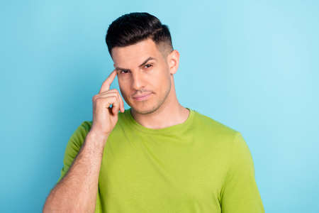 Photo portrait serious man in green t-shirt unhappy keeping finger near forehead isolated pastel blue color backgroundの写真素材