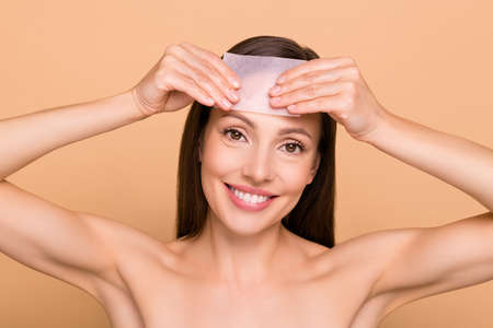 Photo of cute pretty mature woman naked shoulders applying mattifying napkin smiling isolated beige color backgroundの写真素材