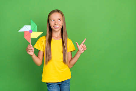 Portrait of attractive cheerful girl holding fan showing copy space isolated over vibrant green color backgroundの写真素材