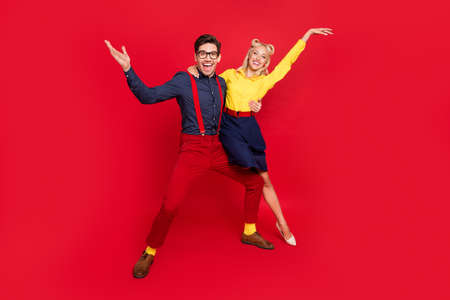 Photo of funny charming young lady guy dressed pinup outfits dancing boogie woogie rising hands arms isolated red color backgroundの写真素材