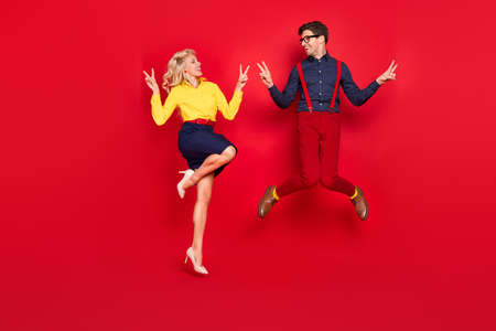 Photo of funky carefree young lady guy dressed pin up 60s outfits jumping high showing v-signs crazy isolated red color backgroundの写真素材