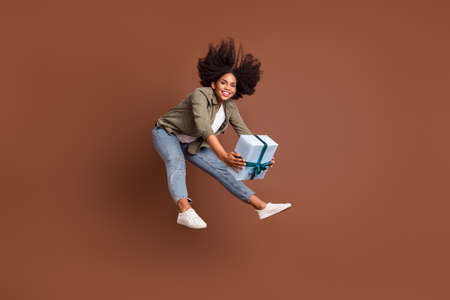 Full length portrait of active cheerful pretty girl hands hold giftbox look camera isolated on brown...