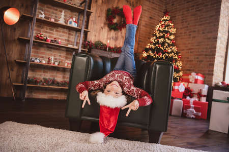 Photo of shiny funny school girl wear print pullover headwear smiling lying armchair showing v-signs indoors house home roomの写真素材
