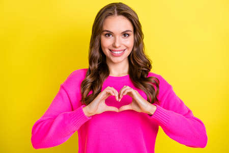 Photo of flirty charming wavy young woman wear pink sweater showing fingers heart isolated yellow...