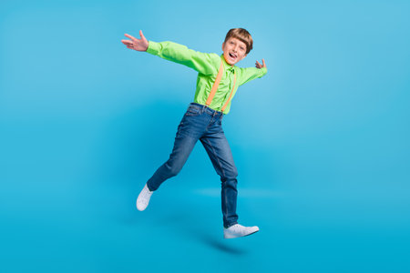 Full size photo of positive cheerful active small boy jump up enjoy weekend smile isolated on blue color backgroundの写真素材