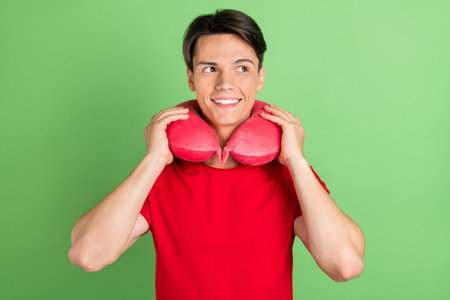 Photo of young guy happy positive smile neck pillow comfort vacation look empty space isolated over green color backgroundの写真素材