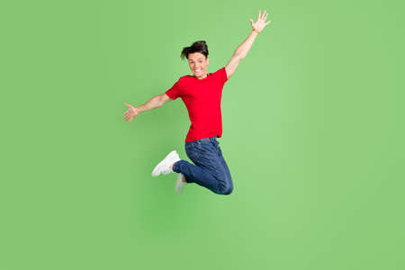 Photo of funky charming young man wear red t-shirt smiling jumping high isolated green color backgroundの写真素材
