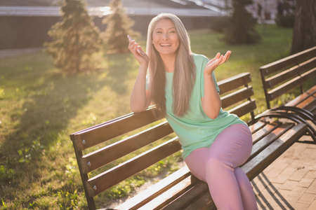 Photo of pensioner lady sit bench hold telephone communicate wear turquoise t-shirt urban city outsideの写真素材
