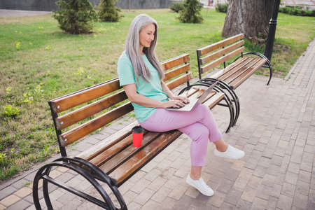 Photo of pensioner lady sit bench freelance remote job netbook wear turquoise t-shirt urban city...