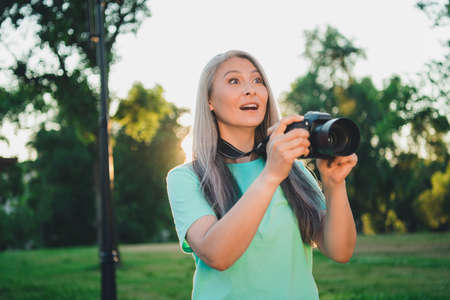 Portrait of attractive amazed cheerful grey-haired woman making photos capture snap having fun shooting outdoorsの写真素材