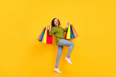 Photo of attractive beautiful afro lady wear green shirt smiling walking holding colorful bargains isolated yellow color backgroundの写真素材