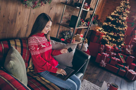 Photo of attractive pretty young lady wear red pullover smiling buying christmas presents modern device indoors house home roomの写真素材