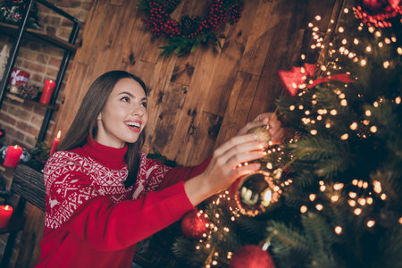 Photo of dreamy shiny young lady wear red pullover smiling decorating christmas tree indoors house home roomの写真素材