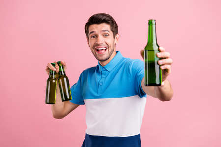 Photo of funny brunet millennial guy hold bottles wear striped polo isolated on pink color backgroundの写真素材
