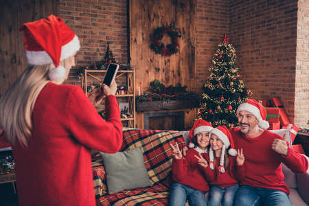 Photo of young woman make snapshot of kids and husband gesture cool v-symbol on smartphone new year advent indoorsの写真素材