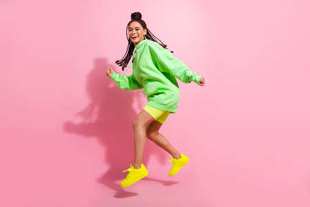 Full body photo of amazed cheerful young dark skin woman jump up go empty space isolated on pink...