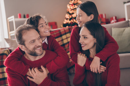 Photo of pretty charming dad mom two children dressed red sweaters embracing smiling indoors room...