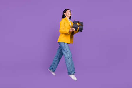 Full body photo of brunette happy cheerful young lady jump hold gift smile isolated on violet color...