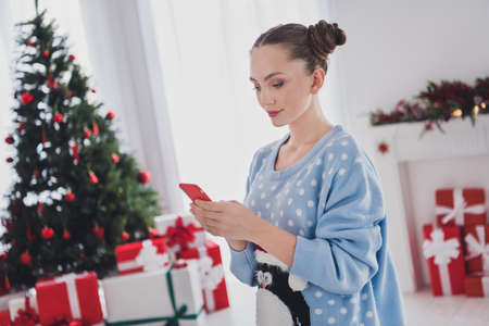 Photo of serious young woman hold hands telephone read message xmas good mood indoors inside houseの写真素材
