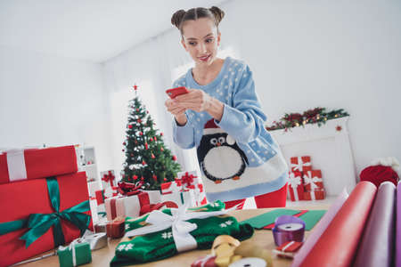 Portrait of attractive focused girl doing craft work blogging preparing gift making taking photo winter day at home indoorsの写真素材