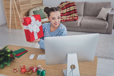 Portrait of beautiful cheerful girl using pc demonstrating giftbox eve time creative day staying at...