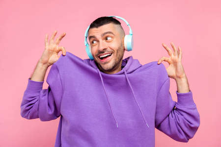 Photo of young funny guy wear hoodie listen playlist earphones look empty space isolated over pink color backgroundの写真素材