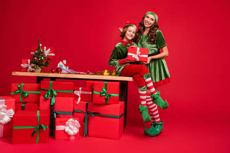 Full length body size view of two attractive cheerful friends elf holding craft giftboxes hugging isolated over bright red color backgroundの写真素材
