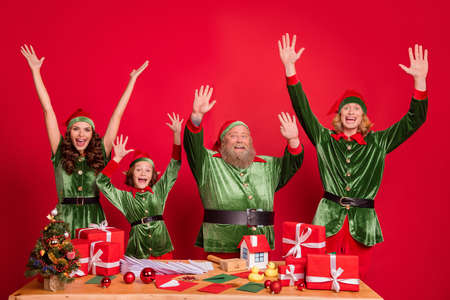 Portrait of four funky trendy cheerful elfs preparing gift dream having fun rising hands up isolated over bright red color backgroundの写真素材