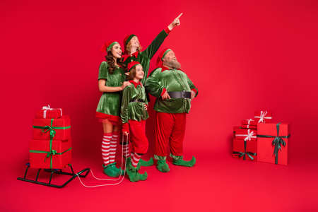 Full size photo of santa helpers people point look empty space with sled giftboxes wear new year costumes isolated on red backgroundの写真素材