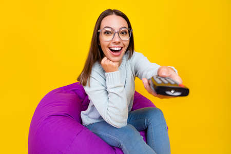 Photo of cheerful amazed young woman tv switch channel remote control isolated on yellow color backgroundの写真素材