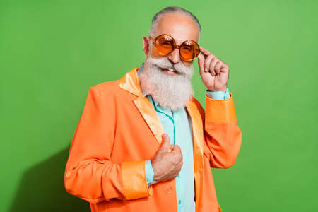 Portrait of attractive cheerful grey-haired man touching orange specs posing isolated over bright green color backgroundの写真素材