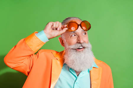 Portrait of attractive dreamy cheerful grey-haired man touching specs thinking isolated over bright green color backgroundの写真素材